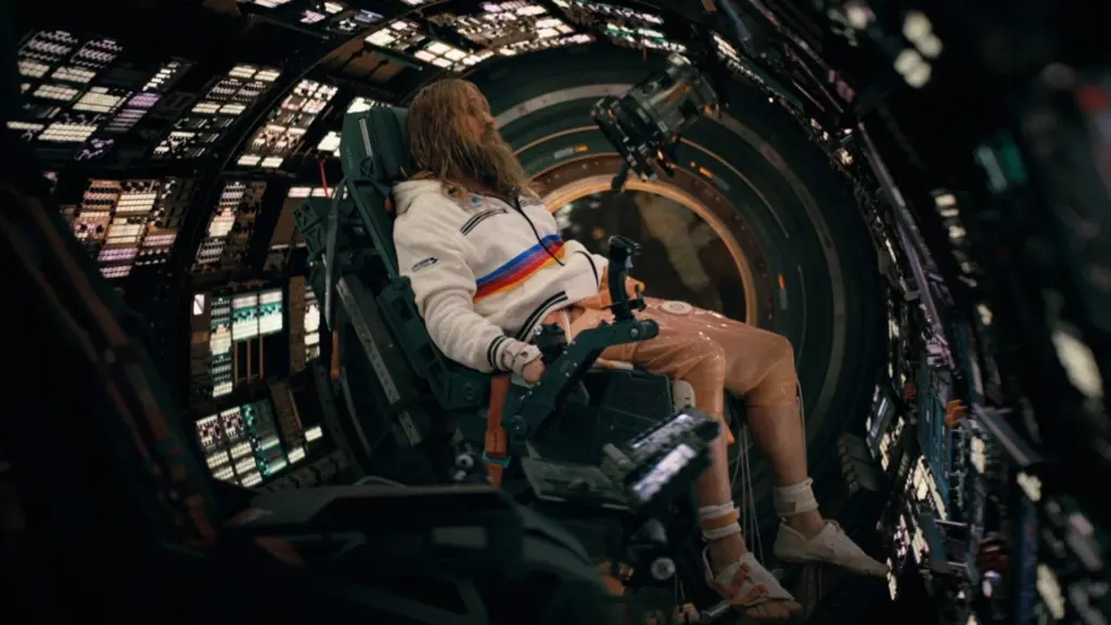 Astronaut seated in a high-tech spacecraft cockpit, surrounded by illuminated control panels and a circular hatch behind.